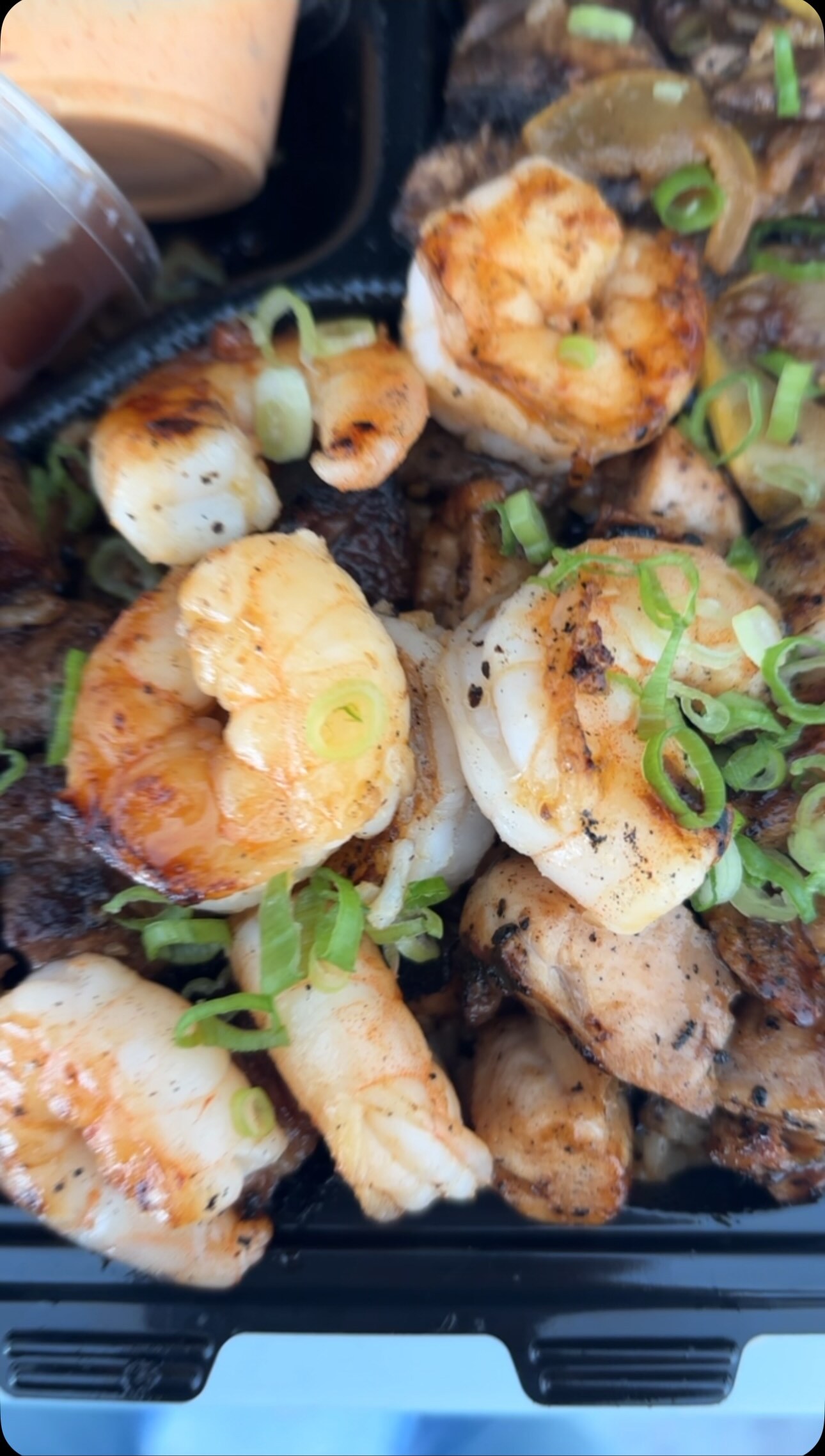 Grilled shrimp over steak and chicken with scallions and yum yum sauce, in a Blue Label to-go box